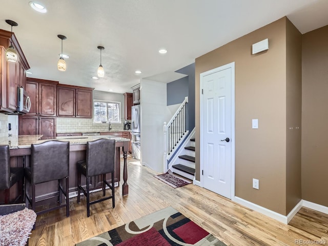 kitchen with appliances with stainless steel finishes, decorative light fixtures, tasteful backsplash, sink, and light wood-type flooring