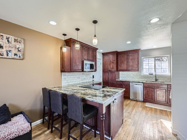 kitchen featuring sink, stainless steel appliances, decorative light fixtures, kitchen peninsula, and light wood-type flooring