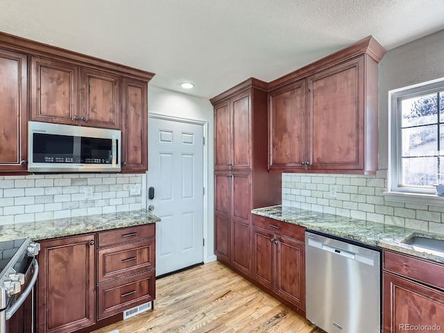 kitchen with light stone counters, decorative backsplash, stainless steel appliances, and light hardwood / wood-style floors