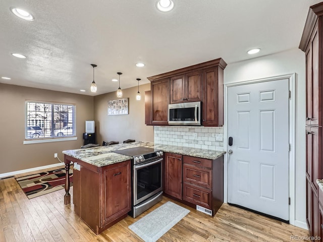 kitchen with stainless steel appliances, decorative light fixtures, kitchen peninsula, and light wood-type flooring