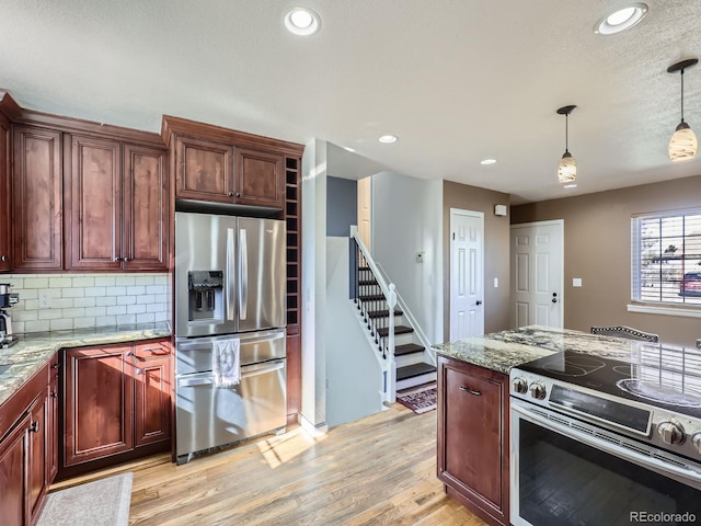 kitchen with light stone counters, stainless steel appliances, decorative light fixtures, and light hardwood / wood-style flooring