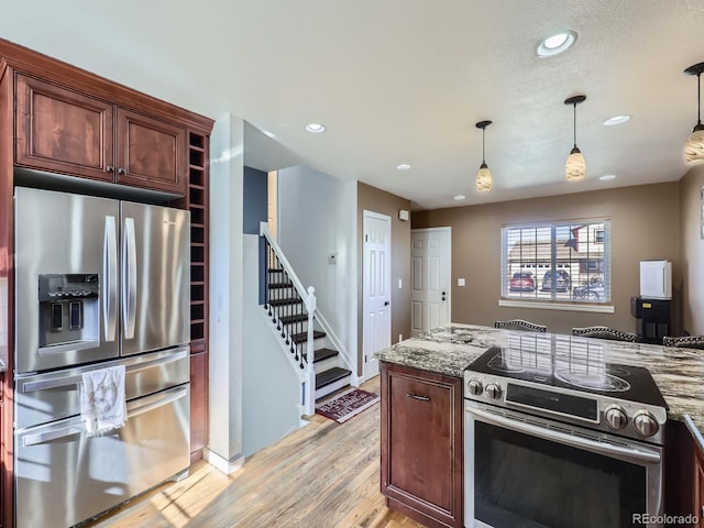 kitchen with appliances with stainless steel finishes, pendant lighting, light stone counters, a textured ceiling, and light wood-type flooring