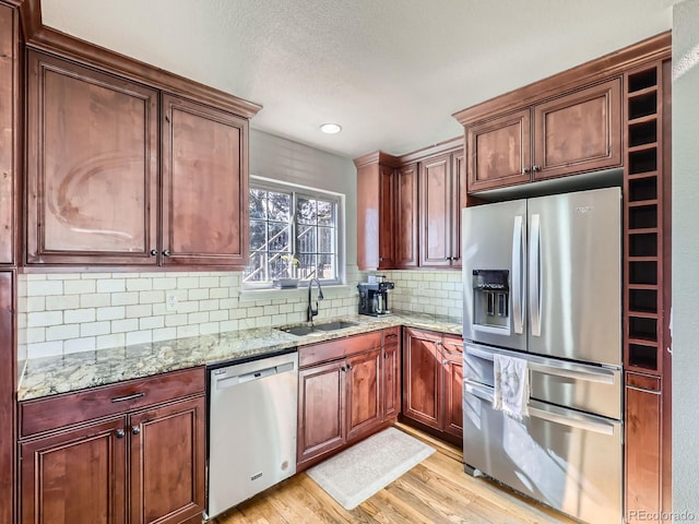 kitchen with sink, appliances with stainless steel finishes, light stone countertops, light hardwood / wood-style floors, and decorative backsplash