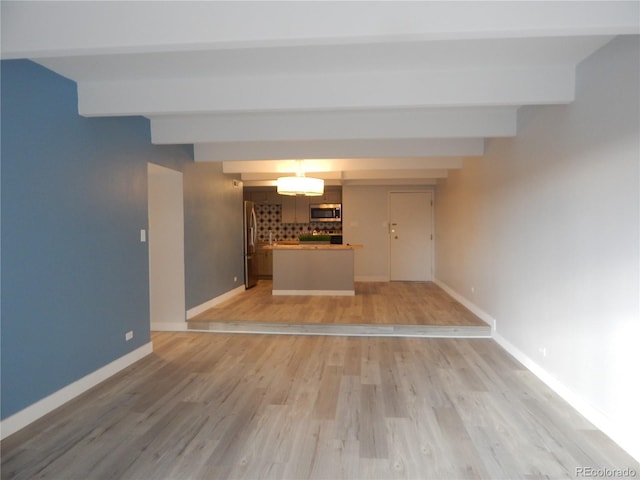 unfurnished living room featuring beamed ceiling and light wood-type flooring