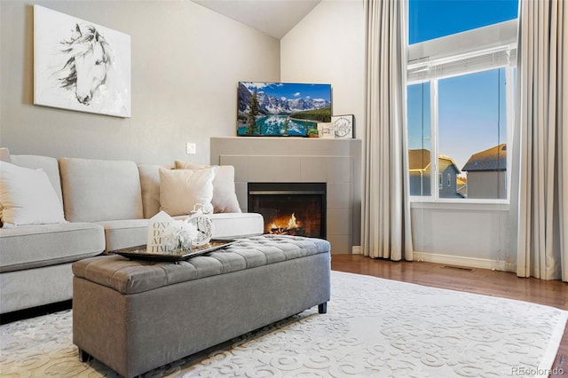 living room featuring vaulted ceiling, a tiled fireplace, and hardwood / wood-style floors