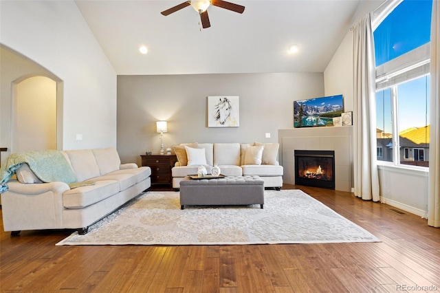 living room with hardwood / wood-style flooring, a tiled fireplace, high vaulted ceiling, and ceiling fan