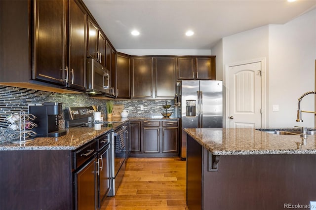 kitchen featuring sink, stone countertops, light wood-type flooring, appliances with stainless steel finishes, and decorative backsplash