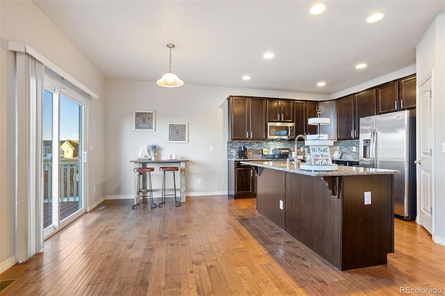 kitchen featuring appliances with stainless steel finishes, a breakfast bar, hanging light fixtures, dark brown cabinetry, and light stone counters