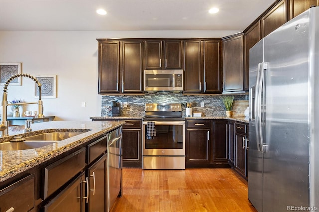 kitchen with sink, light stone counters, light wood-type flooring, stainless steel appliances, and backsplash