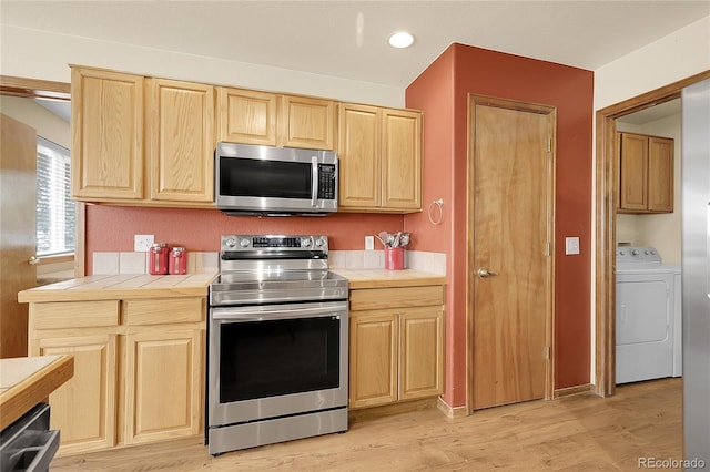 5457 S Valdai St, Aurora, CO 80015 - kitchen featuring stainless steel appliances, washer / dryer, tile counters, light brown cabinetry, and light wood-style flooring