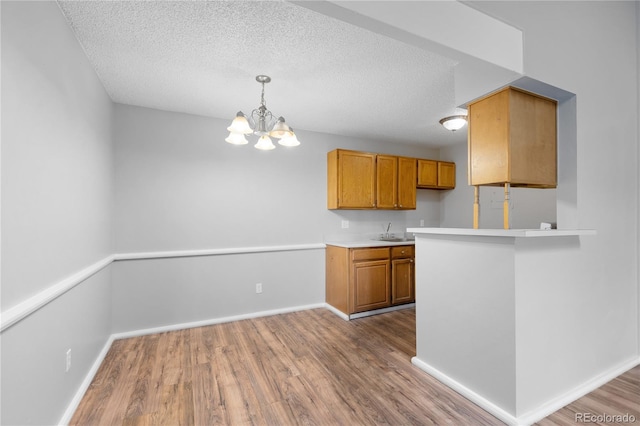 kitchen with a chandelier, pendant lighting, a textured ceiling, and light hardwood / wood-style flooring