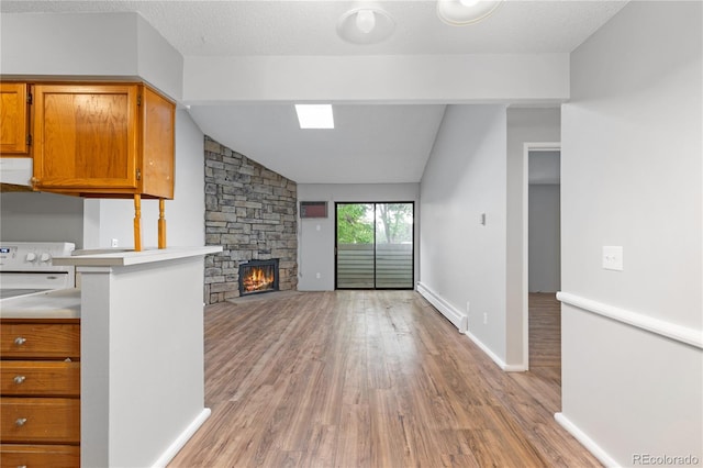 kitchen featuring a baseboard heating unit, a stone fireplace, vaulted ceiling, light wood-type flooring, and kitchen peninsula