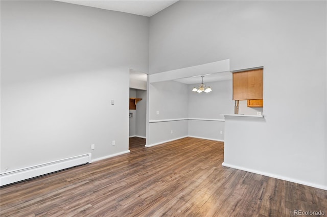 empty room with hardwood / wood-style floors, a towering ceiling, a baseboard radiator, and an inviting chandelier