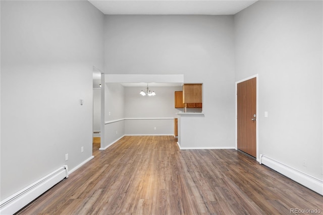 empty room with a towering ceiling, dark hardwood / wood-style floors, an inviting chandelier, and a baseboard heating unit