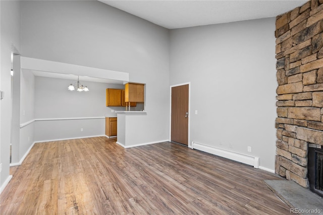 unfurnished living room featuring hardwood / wood-style floors, a stone fireplace, and a baseboard heating unit