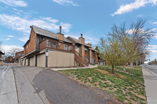 view of side of property with stairway, a chimney, driveway, a shingled roof, and a garage