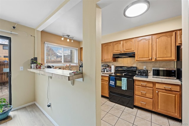 kitchen featuring a peninsula, tasteful backsplash, black appliances, under cabinet range hood, and a breakfast bar area