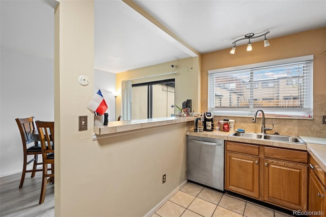 kitchen with light countertops, stainless steel dishwasher, brown cabinets, and a sink