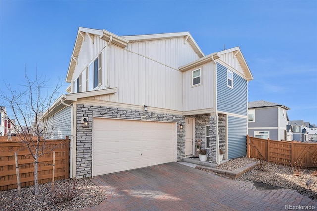 view of front facade with decorative driveway, stone siding, an attached garage, and fence