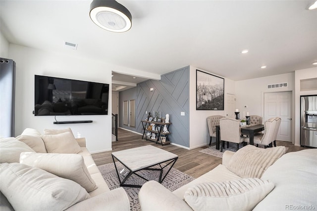 living area with recessed lighting, visible vents, wood finished floors, and an accent wall