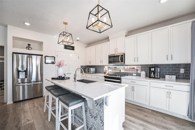 kitchen with a sink, stainless steel appliances, light wood-type flooring, and backsplash