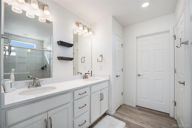 full bath with double vanity, wood finished floors, a stall shower, and a sink