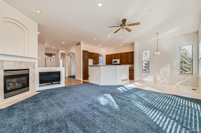 unfurnished living room with arched walkways, recessed lighting, a tiled fireplace, and ceiling fan with notable chandelier