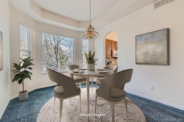 carpeted dining room with a raised ceiling, baseboards, visible vents, and arched walkways