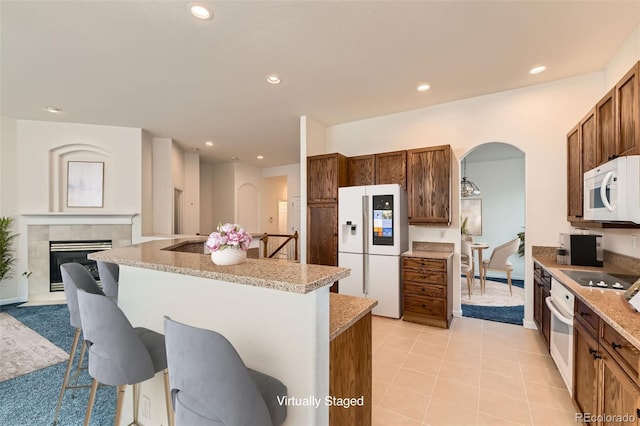 kitchen with a breakfast bar, an island with sink, recessed lighting, arched walkways, and white appliances