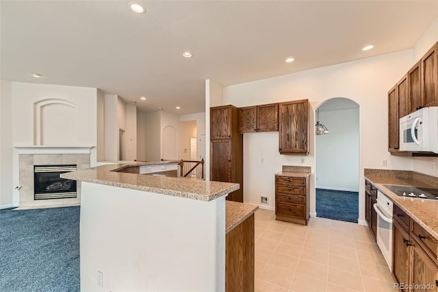 kitchen featuring light carpet, recessed lighting, white appliances, arched walkways, and a tile fireplace