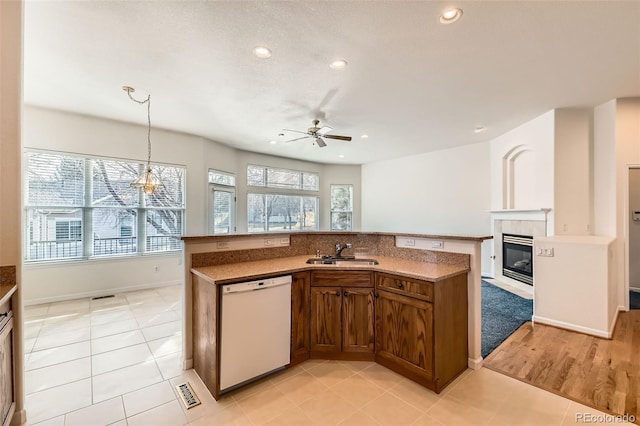 kitchen featuring visible vents, a tiled fireplace, white dishwasher, hanging light fixtures, and a sink