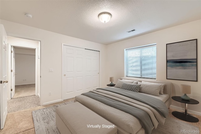 bedroom with visible vents, a textured ceiling, a closet, baseboards, and light colored carpet