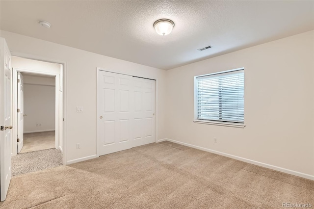 unfurnished bedroom with visible vents, a textured ceiling, a closet, baseboards, and light colored carpet