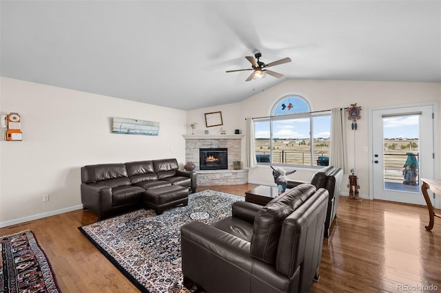 living room with baseboards, vaulted ceiling, a fireplace, wood finished floors, and a ceiling fan