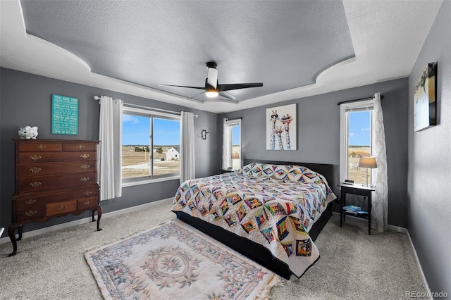 carpeted bedroom featuring baseboards, a textured ceiling, a raised ceiling, and ceiling fan