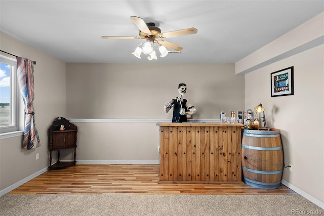 bar featuring baseboards, wood finished floors, bar area, and ceiling fan