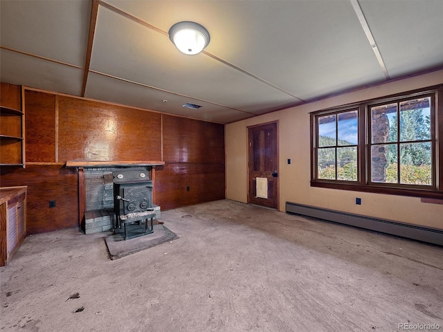 unfurnished living room with a wood stove, wooden walls, light colored carpet, and a baseboard radiator