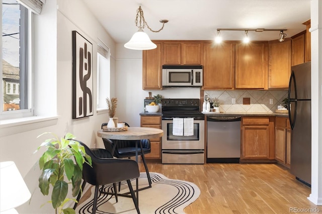 kitchen with stainless steel appliances, light wood-type flooring, tasteful backsplash, and pendant lighting