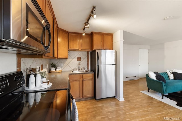 kitchen with sink, tasteful backsplash, light hardwood / wood-style flooring, a baseboard heating unit, and appliances with stainless steel finishes