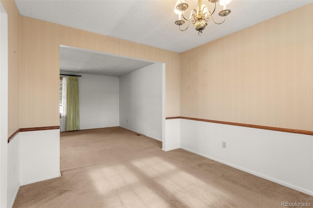 unfurnished room featuring carpet flooring, a textured ceiling, and a notable chandelier