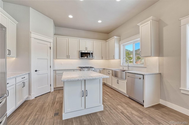 kitchen featuring sink, white cabinetry, light wood-type flooring, appliances with stainless steel finishes, and light stone countertops