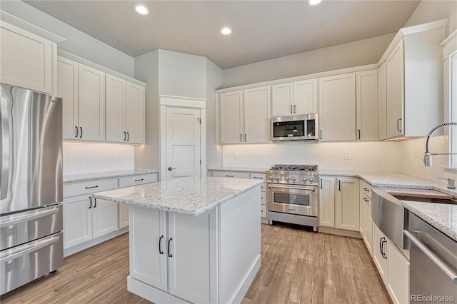 kitchen with light stone counters, stainless steel appliances, white cabinets, and light wood-type flooring