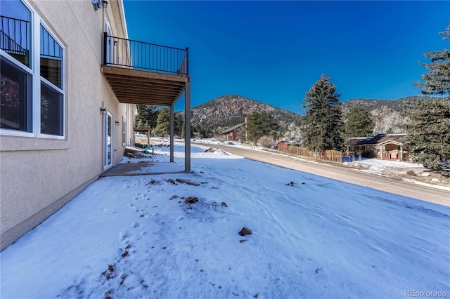 yard covered in snow featuring a mountain view and a balcony