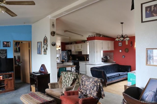 living room featuring vaulted ceiling, ceiling fan with notable chandelier, and light hardwood / wood-style flooring