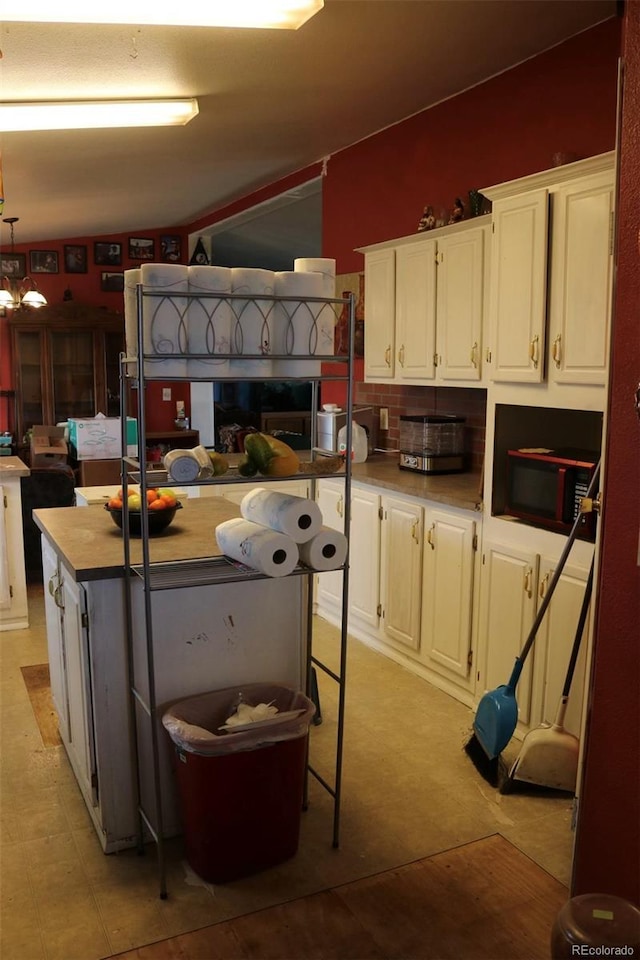 kitchen with a center island, backsplash, white cabinetry, and a notable chandelier