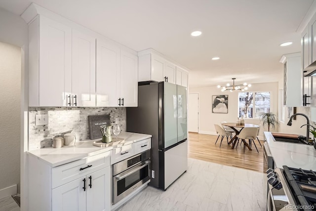 kitchen featuring white cabinetry, appliances with stainless steel finishes, backsplash, light stone countertops, and sink