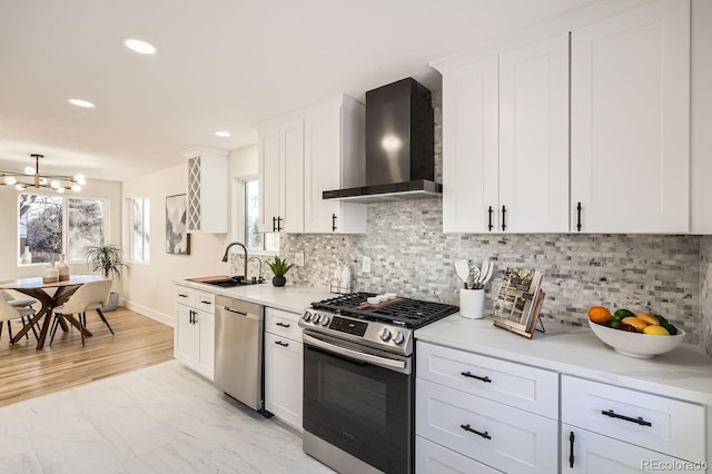 kitchen featuring appliances with stainless steel finishes, white cabinetry, wall chimney range hood, decorative backsplash, and sink