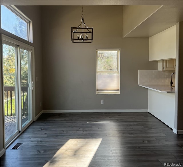 unfurnished dining area featuring dark wood-style floors, visible vents, a sink, a chandelier, and baseboards