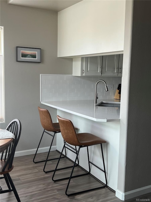 kitchen with a sink, light countertops, gray cabinets, tasteful backsplash, and a kitchen bar