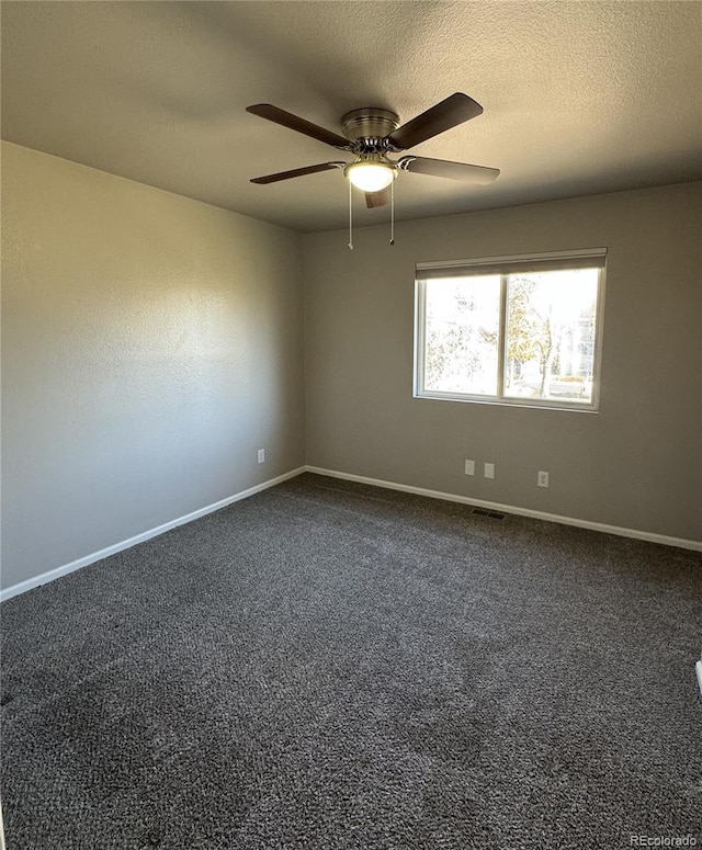 empty room featuring a ceiling fan, dark carpet, a textured ceiling, and baseboards